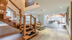 A modern interior with a wooden staircase, a cozy seating area, and a kitchen visible through an open space. - 10 Bed in Howtown (oc-w33505) (Ullswater)