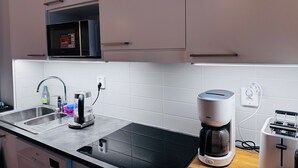 Une cuisine moderne équipée d’une plaque de cuisson à induction noire, d’une machine à café, d’un grille-pain et d’un four à micro-ondes.