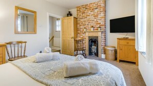 A bedroom with a large bed, a fireplace, a television, and a wooden wardrobe. - 3 Bed in Wells-next-the-Sea (oc-h33452) (Wells-next-the-Sea)