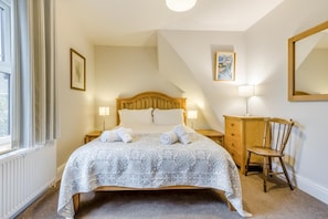 Quarto com cama, mesa de cabeceira, cadeira de madeira, cômoda, abajur e quadro na parede.