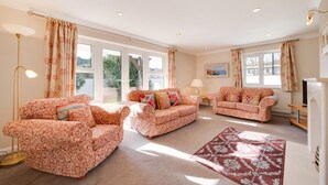A spacious living room with floral-patterned sofas, a red rug, and a television. - 4 Bed in Shaldon (oc-sunnhs) (Shaldon)