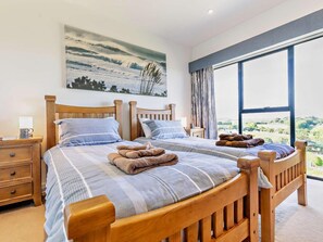 Una cama doble con cabecero de madera, dos mesitas de noche, un aparador, un ventanal con vistas y un cuadro en la pared.