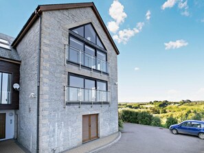 Un edificio de dos pisos con fachada de piedra, ventanas grandes y un coche estacionado adelante.