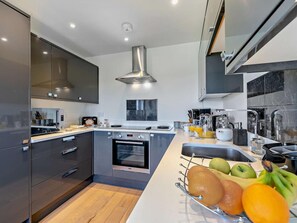 Una cocina moderna con armarios oscuros, una campana extractora de acero inoxidable, un horno empotrado y un frutero sobre la encimera.