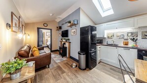 Eine moderne Wohnung mit Wohnzimmer, Küche und Essbereich. Sie verfügt über einen Kamin, einen schwarzen Kühlschrank und einen Esstisch mit Stühlen.
