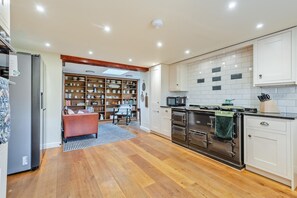 A modern kitchen with built-in appliances, a dining area with a sofa, and a large bookshelf. - 4 Bed in Ellonby (oc-y33284) (Ellonby)