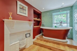 A bathroom with a freestanding bathtub, a window with a view, and a red wall with a framed picture. - 4 Bed in Ellonby (oc-y33284) (Ellonby)