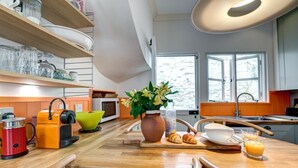 Une cuisine avec des plans de travail en bois, un four à micro-ondes, une bouilloire, un vase rempli de fleurs et un verre de jus d’orange.