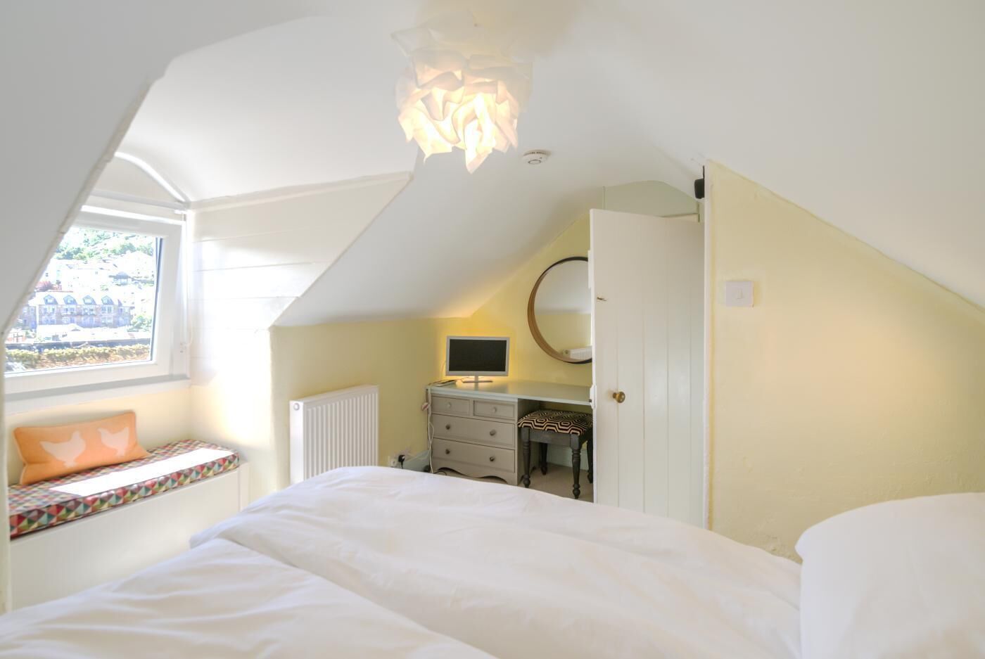 Une chambre à coucher avec un lit, un bureau avec un ordinateur, une fenêtre donnant sur un paysage agréable et un radiateur.