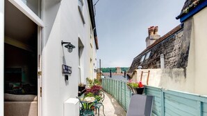 Une ruelle étroite, avec un bâtiment blanc d’un côté et un bâtiment peint en bleu de l’autre. On y trouve un petit espace extérieur aménagé avec une table et des chaises, ainsi qu’une enseigne indiquant « La Petite Maison Blanche ».