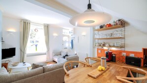 Un salon moderne comprenant un canapé, une table à manger et un coin cuisine avec des étagères et des appareils électroménagers.