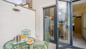 Une terrasse avec une table et des chaises, une porte-fenêtre coulissante donnant sur une pièce et un petit espace extérieur aménagé pour s’asseoir.