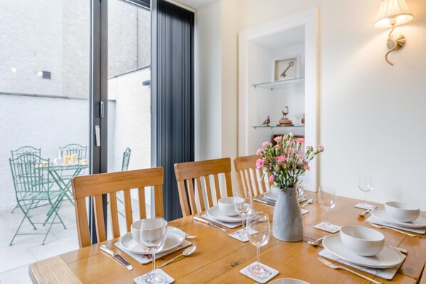 A dining table set for four with chairs, a vase of flowers, and a glass shelf with decorative items. - 4 Bed in Kelso (oc-b33446) (Kelso)