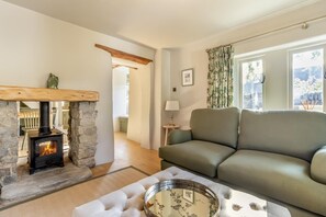 Ein Wohnzimmer mit Kamin aus Stein, einer Couch und Blick durch ein Fenster.
