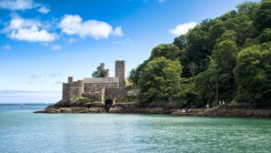 Eine historische Burg an einer felsigen Küste mit klarem, blauem Wasser und üppigem Grün.