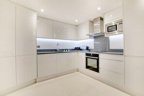 A modern kitchen with white cabinets, a built-in oven, a microwave, and a stainless steel range hood. - 2 Bed in Dartmouth (oc-bcsail) (Dartmouth)