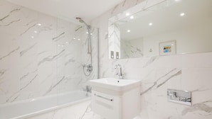 Ein modernes Badezimmer mit Marmorboden, einer freistehenden Badewanne, einem Waschtisch und einem großen Spiegel.