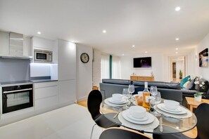 A modern kitchen with built-in appliances, a dining area with a glass table set for four, and a living area with a sofa and a flat-screen TV. - 2 Bed in Dartmouth (oc-bcsail) (Dartmouth)