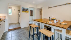 Une cuisine avec une table en bois, des tabourets de bar, une cafetière et un panneau accroché au mur.