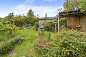 Un jardin avec un rocher, une structure en bois et une mangeoire à oiseaux.