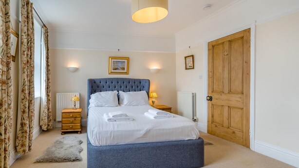 Une chambre avec un grand lit, des tables de chevet en bois, un radiateur et une porte en bois.