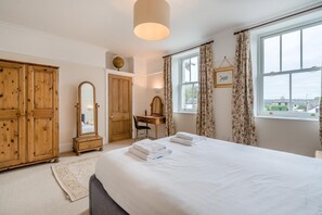 Et soveværelse med en seng, et træskab, et skrivebord med stol, et spejl og et vindue med gardiner.