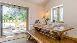 Un'area pranzo con un tavolo in legno apparecchiato per quattro persone, una panca e vista sull'esterno tramite una porta scorrevole in vetro.