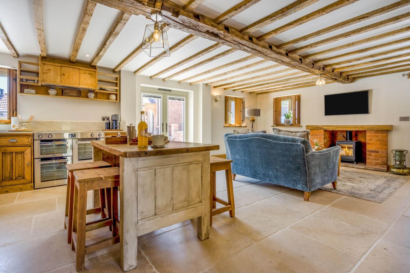 A rustic kitchen with wooden beams, a dining area with a blue sofa, and a fireplace.