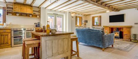 A rustic kitchen with wooden beams, a dining area with a blue sofa, and a fireplace.