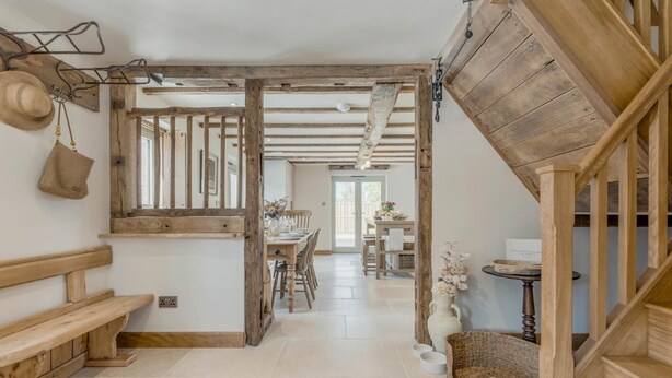 Een rustiek interieur met zichtbare houten balken, een houten bank, een eethoek en een trap.