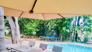 An outdoor dining area with a table and chairs under a canopy, a pool in the background, and a natural setting with trees and rocks. - Executive comfort with premium workspace - 2334 (Kwekwe)