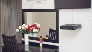 A modern room with a dark wooden table, a white vase with red and white flowers, a chair, a flat-screen TV mounted on the wall, and a small black shelf. - Executive comfort with premium workspace - 2334 (Kwekwe)