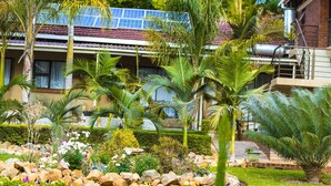Une maison dotée de panneaux solaires, un jardin avec différentes espèces de plantes et une façade en briques.