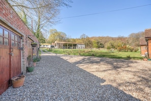 A gravel driveway leading to a brick building with a red door, a covered outdoor area, and a fenced field.