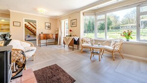 A spacious living area with a fireplace, wicker furniture, and large windows offering a view of the outdoors.