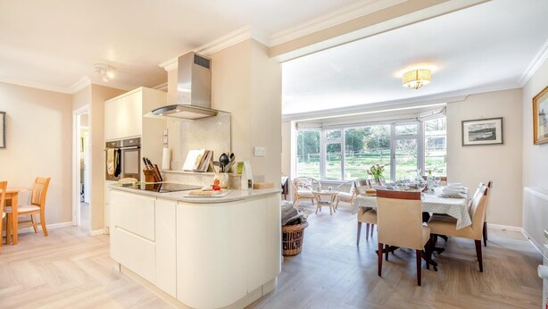 A modern kitchen with a central island, dining area with chairs, and large windows.