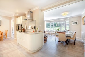 A modern kitchen with a central island, dining area with chairs, and large windows.