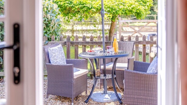 Een terras buiten met rieten meubels, een ronde tafel en een fles sinaasappelsap.