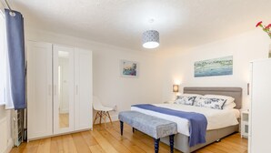 Een slaapkamer met een bed, nachtkastje, lamp, stoel, kast en kunstwerk aan de muur.