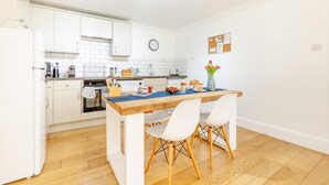 Een compacte keuken met witte kastjes, een houten eettafel en een klein eiland.