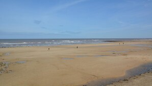 Een breed zandstrand met een heldere lucht en een rustige zee.