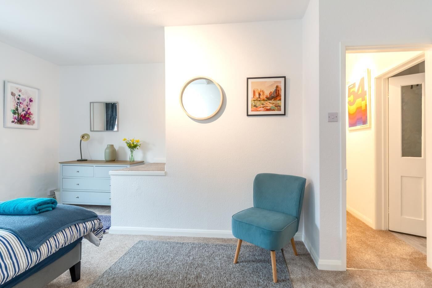 Ein Schlafzimmer mit einem Bett, einer Kommode, einem Stuhl, einem runden Spiegel und zwei gerahmten Bildern an der Wand.