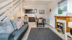 Ett modernt vardagsrum med en grå soffa, en öppen spis och en trappa som leder upp till en övre våning.