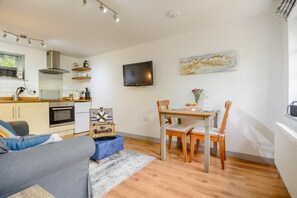 A compact living space with a kitchenette, a dining area with a table and chairs, a sofa, and a television mounted on the wall. - 1 Bed in West Runton (oc-1718) (West Runton)