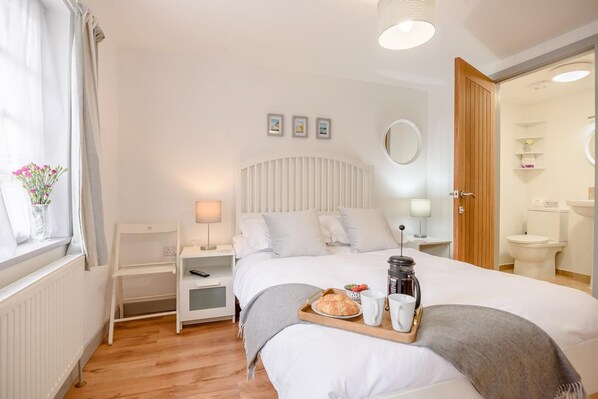 A hotel room with a bed, bedside tables, a window with curtains, a bedside lamp, a tray with breakfast items, and a coffee maker. - 1 Bed in West Runton (oc-1718) (West Runton)