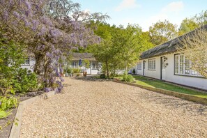 A traditional white building with a gravel courtyard, surrounded by lush greenery and flowering trees. - 1 Bed in West Runton (oc-1718) (West Runton)