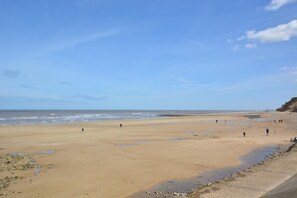 A wide sandy beach with a calm sea, a few people walking, and a cliff on the right. - 1 Bed in West Runton (oc-1718) (West Runton)