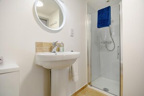A bathroom with a white sink, a mirror, a glass shower enclosure, and a towel hanging on the wall. - 1 Bed in West Runton (oc-1718) (West Runton)