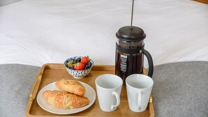 Ein Tablett mit Croissants, einer Obstschale und einer Kaffeemaschine auf einem Bett.
