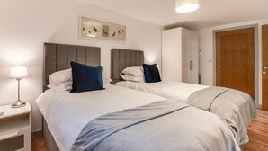 Een hotelkamer met twee bedden, een nachtkastje met een lamp, een kunstwerk aan de muur en een deur.